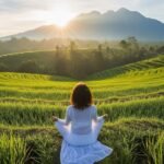 Seorang perempuan sedang bermeditasi di tengah sawah pada pagi hari