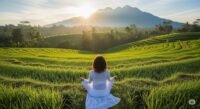 Seorang perempuan sedang bermeditasi di tengah sawah pada pagi hari